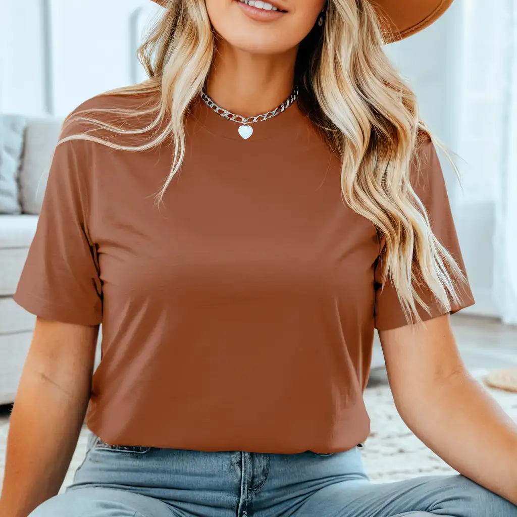blonde woman wearing bella canvas 3001 heather clay t-shirt mockup, with hat and silver necklace, simple boho home background, sitting on the floor
