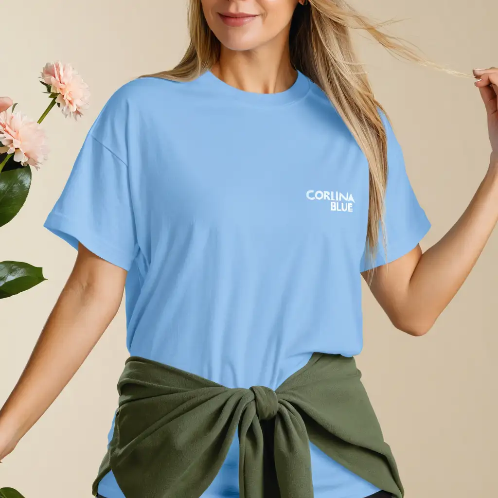 Blonde woman wearing gildan 5000 carolina blue oversized t-shirt mockup, holding flower, with flowers on the background, body facing front