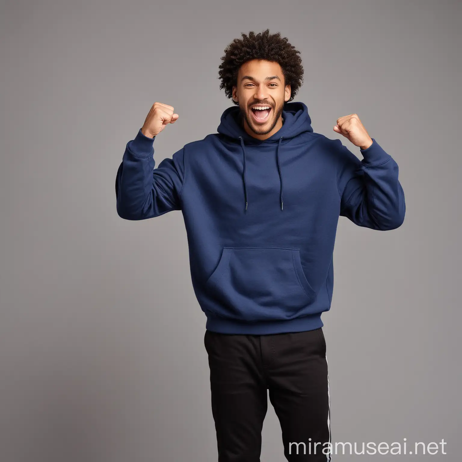 Excited  black curly guy cheerfully smiling, putting on dark blue sweatshirt and black pants , raising clenched fist up , shouting with energy to victory , standing against gray space , in front of camera